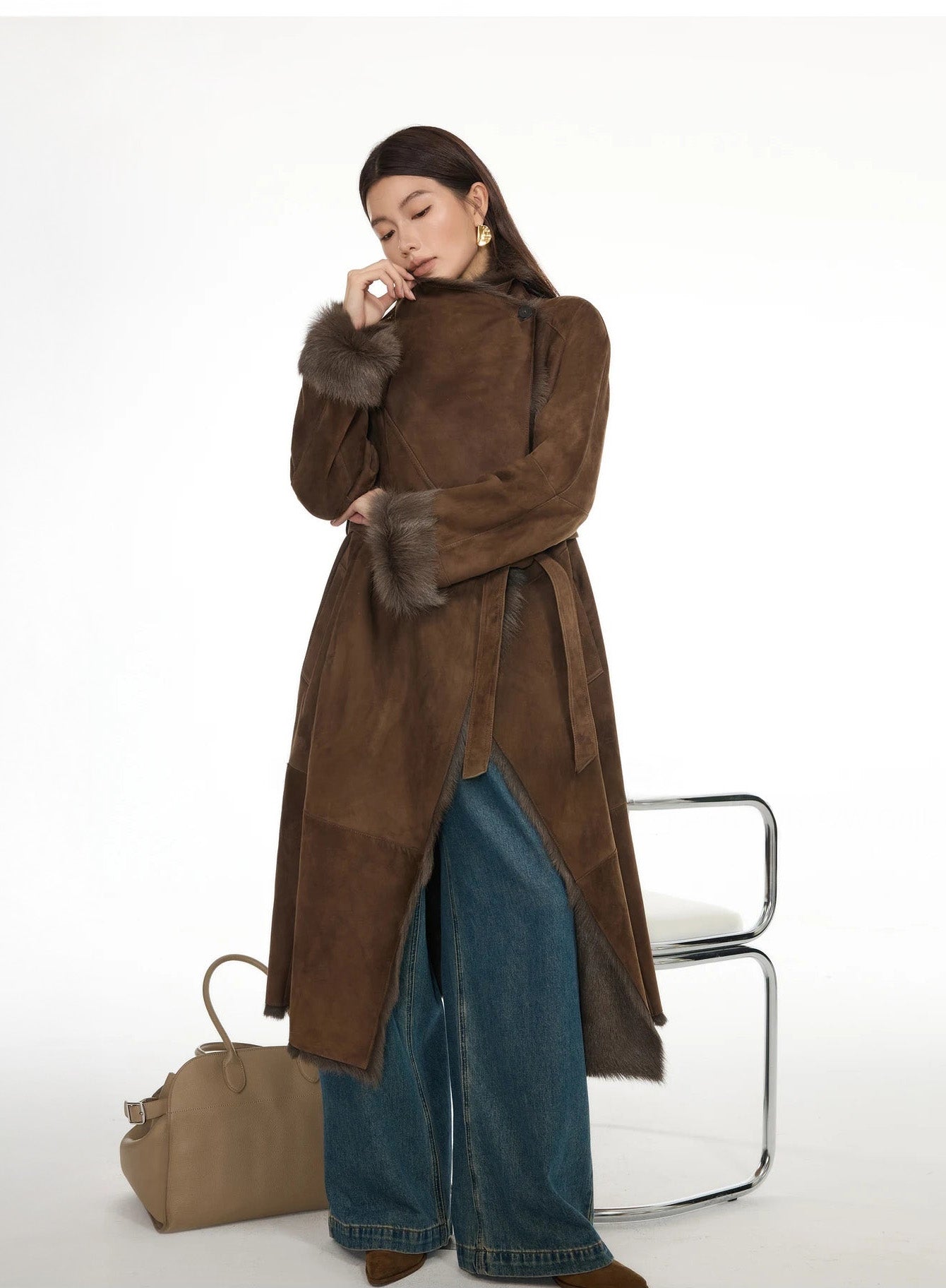 Model touching the fastened collar of the Woodsy Brown goatskin coat, emphasizing the large lapel and structured shape — From Borcelleclothes.