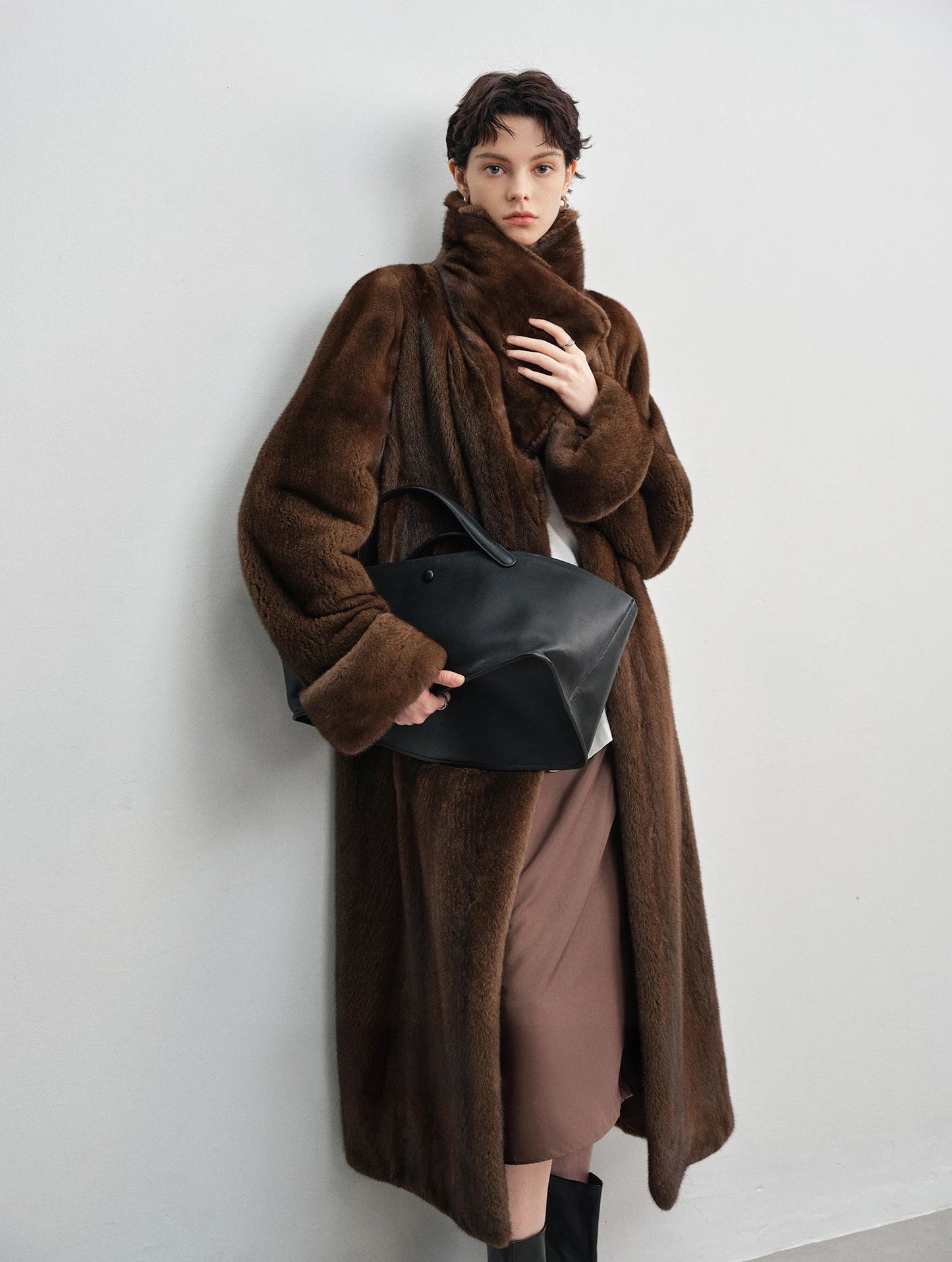 Model leaning against a white wall in the brown mink coat — From Borcelleclothes.