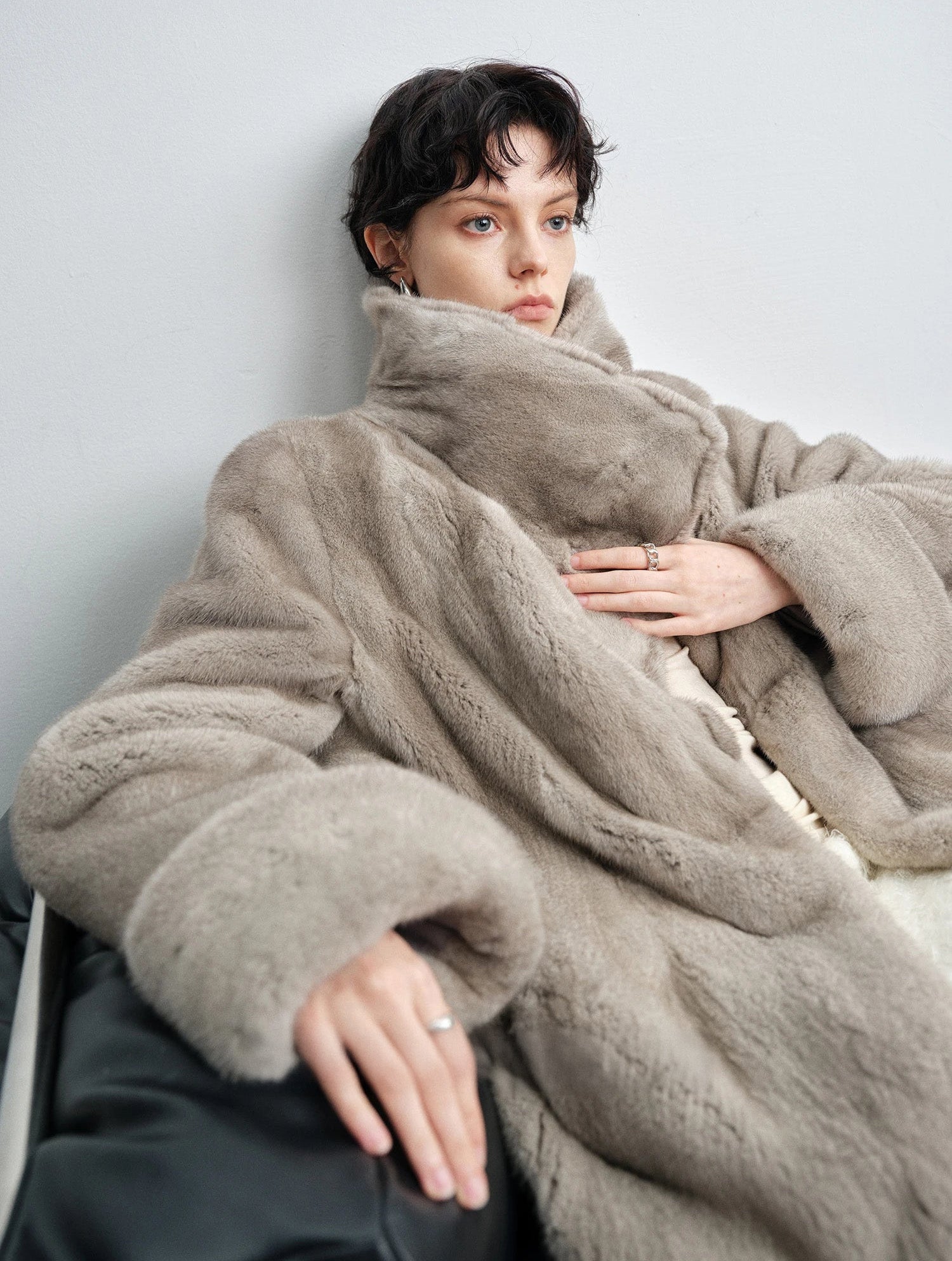 Seated model gently holding both lapels of the silver blue mink coat together — From Borcelleclothes.