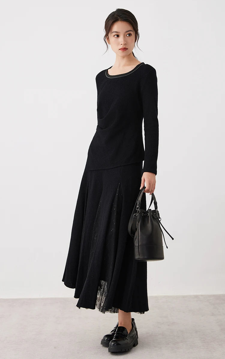 Full-height view of a model holding a black bag, wearing a women's wool godet skirt with sheer panels in Game in Black — From Borcelleclothes.