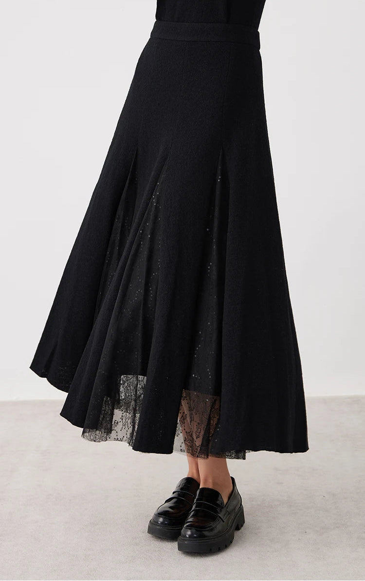 Model swirling to display the dramatic lace-overlaid sheer panels of a women's wool godet skirt in Game in Black — From Borcelleclothes.