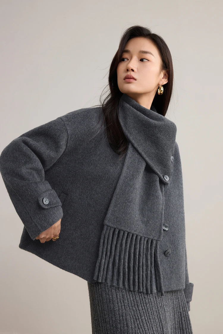 A woman poised with her forearm raised, showcasing the soft drape of the grey wool scarf — From Borcelleclothes.