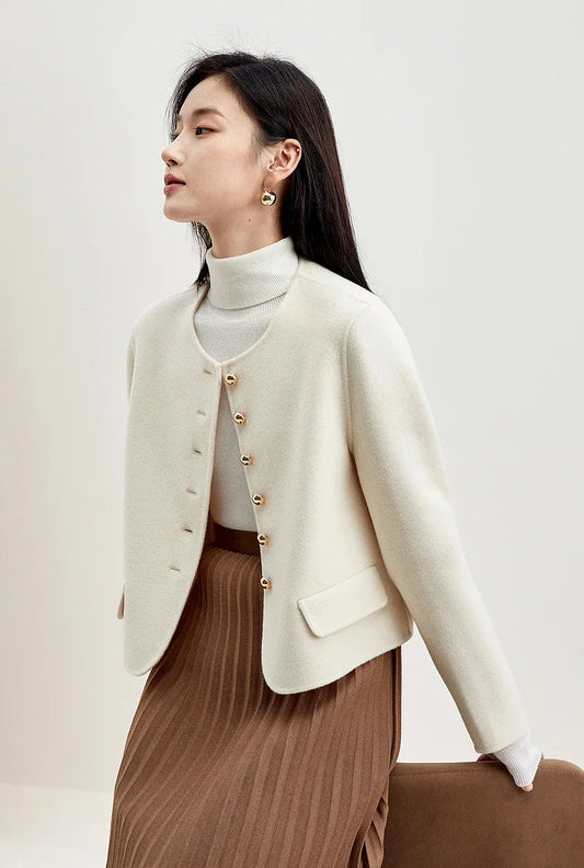 Woman in a cream wool jacket sitting elegantly on the back of a chair, showing the fluid drape of the double-sided fabric — From Borcelleclothes.