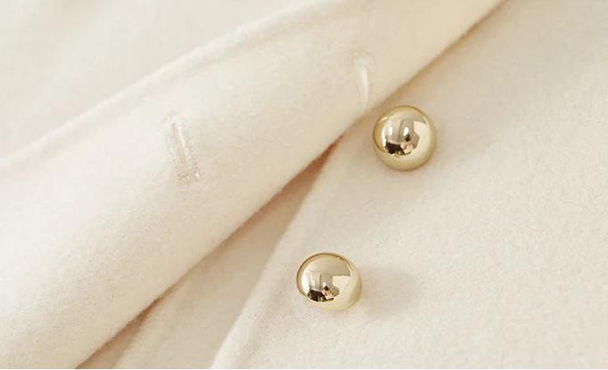Macro shot of two unfastened golden sphere buttons against the delicate cream wool — From Borcelleclothes.