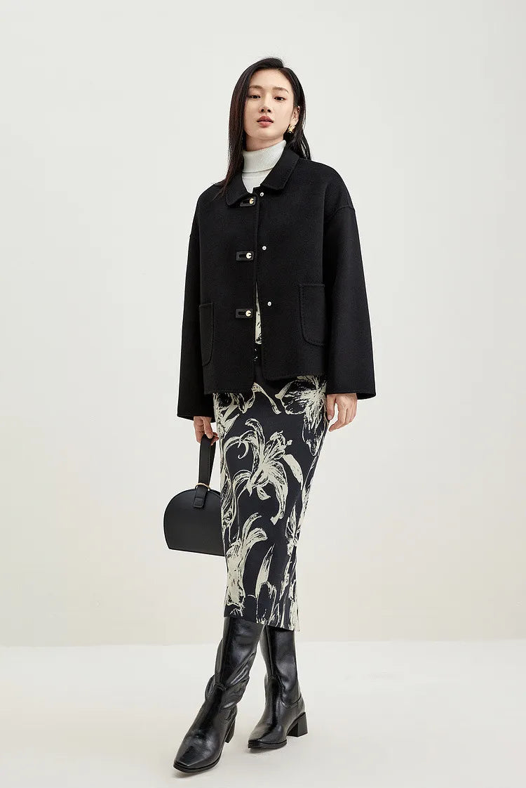 Model with crossed legs in a black women's wool jacket with graphic loop detail — From Borcelleclothes.