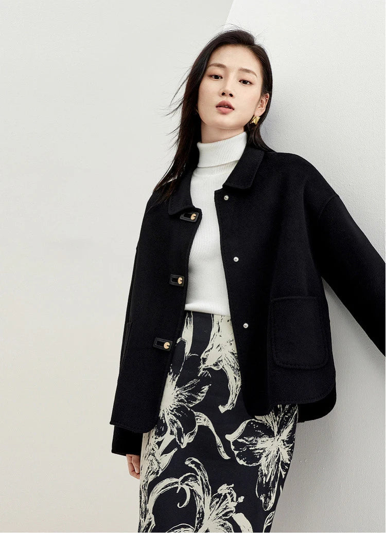 A woman leaning against a wall in a black wool jacket with graphic loop detail — From Borcelleclothes.