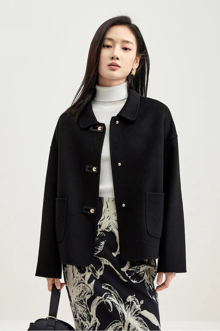 A woman holding an oversized bag, wearing an unfastened black wool jacket with graphic loop detail — From Borcelleclothes.