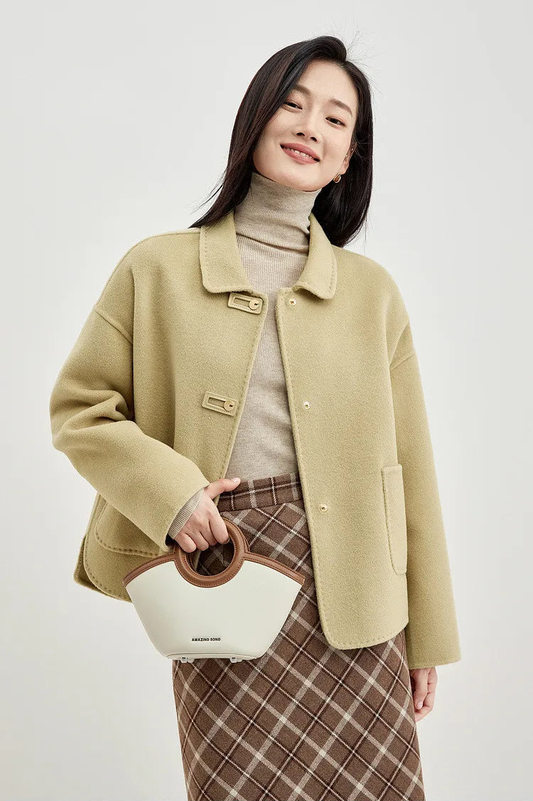 A woman holding a small bag, wearing a wool jacket with graphic loop detail — From Borcelleclothes.