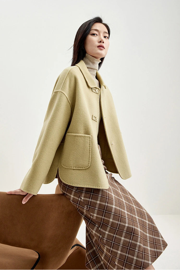 Side view of a woman perched on an armchair in a wool jacket with graphic loop detail — From Borcelleclothes.