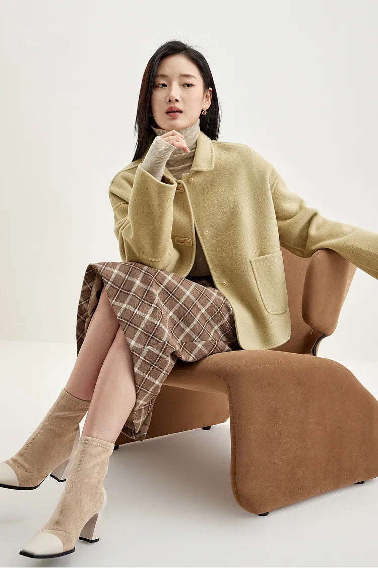 Seated woman touching her chin, wearing a wool jacket with graphic loop detail — From Borcelleclothes.