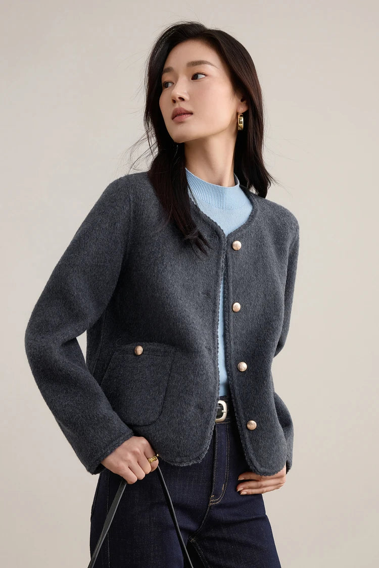 A woman turned slightly to the side in a Perle Noir wool jacket, showing the clean lines of the tailored armholes and hip-length cut. — From Borcelleclothes.