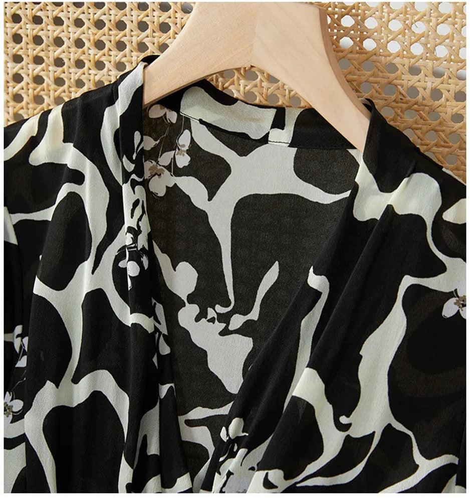 The sharp V-neckline of the wrap bodice, accentuating the neck's grace against the background of abstract, ink-like flowers. — From Borcelleclothes.