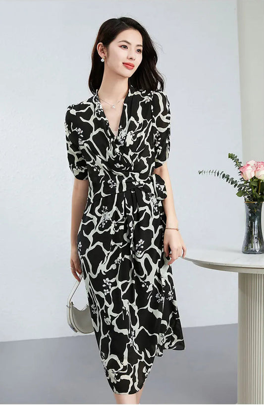 A woman holding a white bag, standing in a midi wrap dress made of 100% Mulberry silk. The monochrome "Rorschach" print creates a sharp contrast, embodying quiet confidence. — From Borcelleclothes.