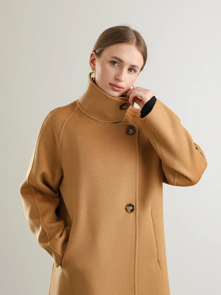 A woman finds comfort in the fastened high collar of her Camel Train coat from Borcelleclothes, a shield of warmth for her journey.