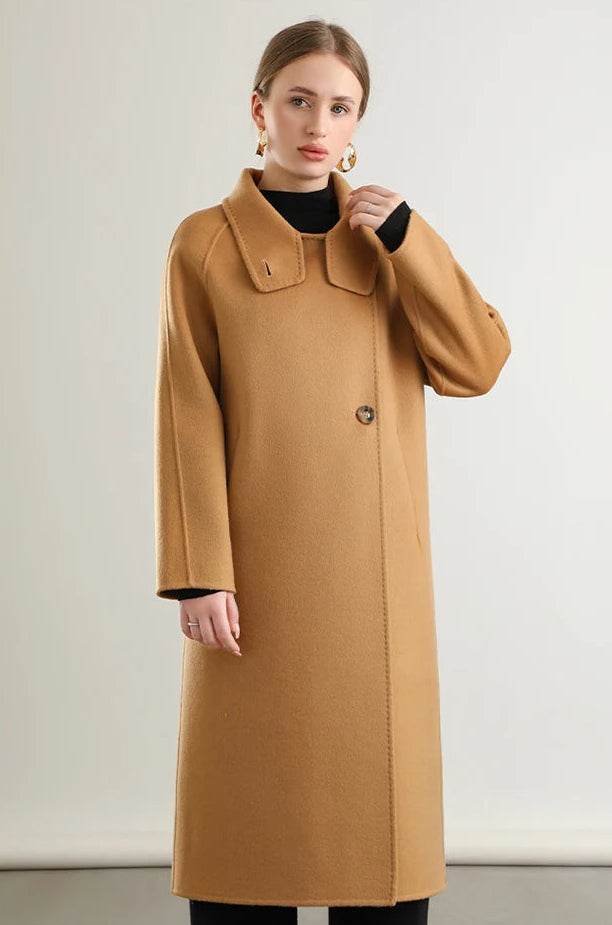 The relaxed elegance of the Camel Train coat from Borcelleclothes, with a woman’s hand highlighting the effortless drape of the unfastened wool.
