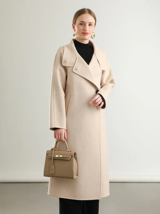 A woman gracefully holding a handbag, draped in the Ivory Route wrap coat from Borcelleclothes, embodying the purity and luxury of a timeless journey. 
