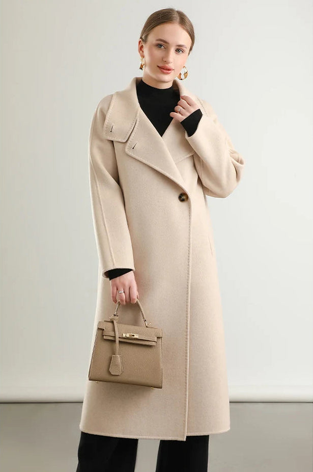 A moment of quiet reflection as a woman touches the unfastened collar of her Ivory Route coat from Borcelleclothes, showcasing the soft flow of double-sided wool.