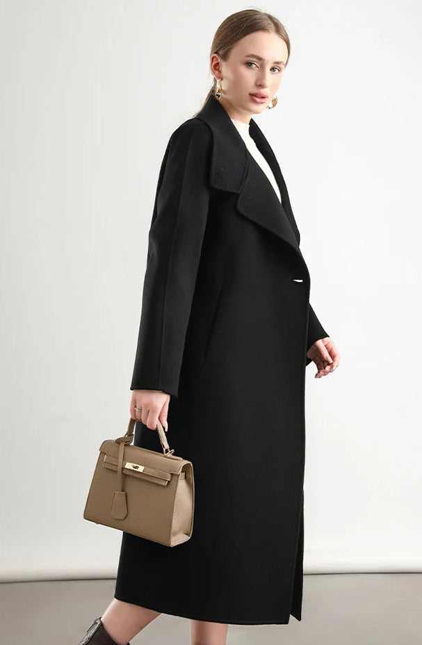 A woman walking in profile, her Kohl Night coat from Borcelleclothes trailing like a soft shadow in the evening light.