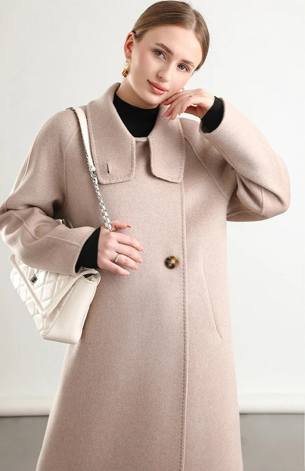 A feminine gesture as a woman in the Sultana Spice coat from Borcelleclothes touches her cheek, the amber-pink hue of the wool reflecting a warm, sun-soaked glow.