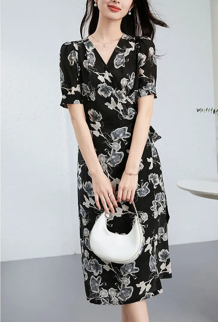 Sophisticated woman holding a white handbag with both hands, highlighting the contrast against the textured black silk wrap dress — From Borcelleclothes.