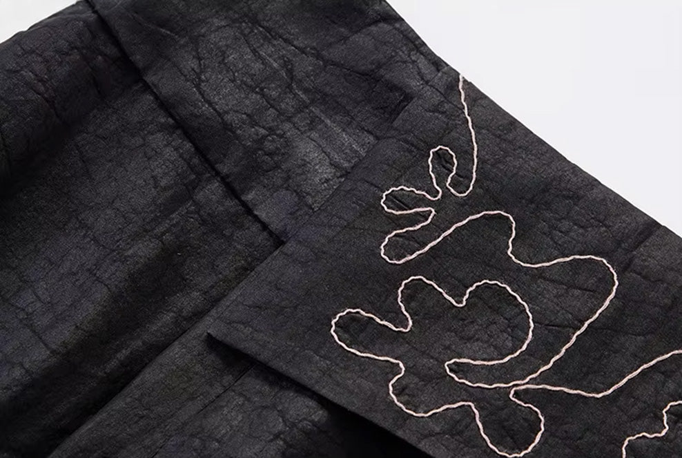 Macro shot of the asymmetric front overlay panel adorned with intricate, abstract embroidery — From Borcelleclothes.