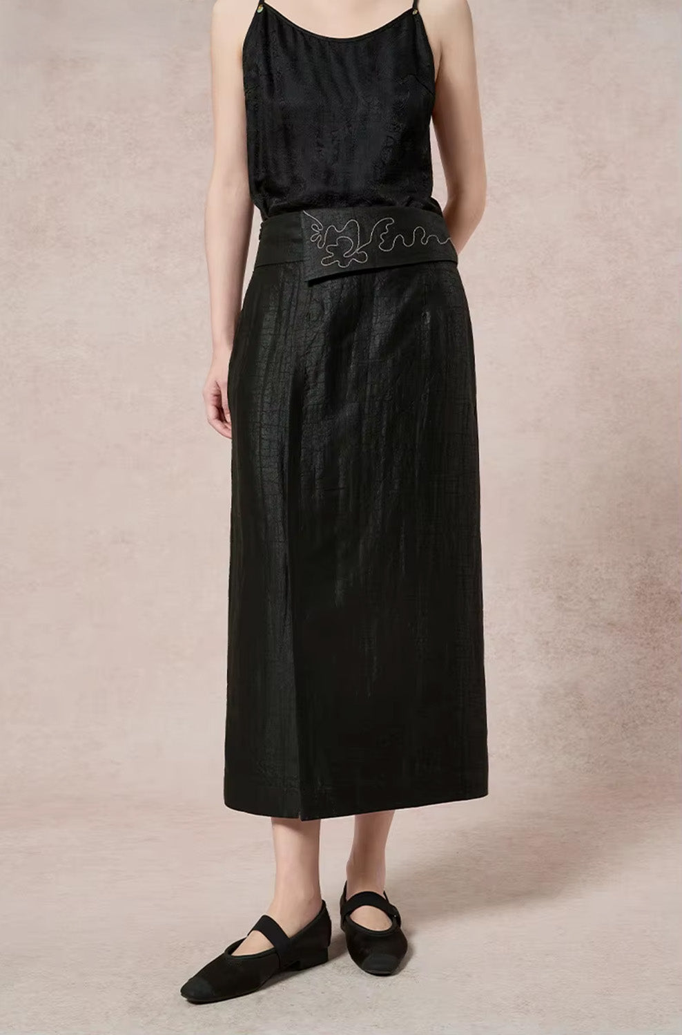 Mid-shot profile view focusing on the clean lines and silhouette of the structured black silk midi skirt — From Borcelleclothes.