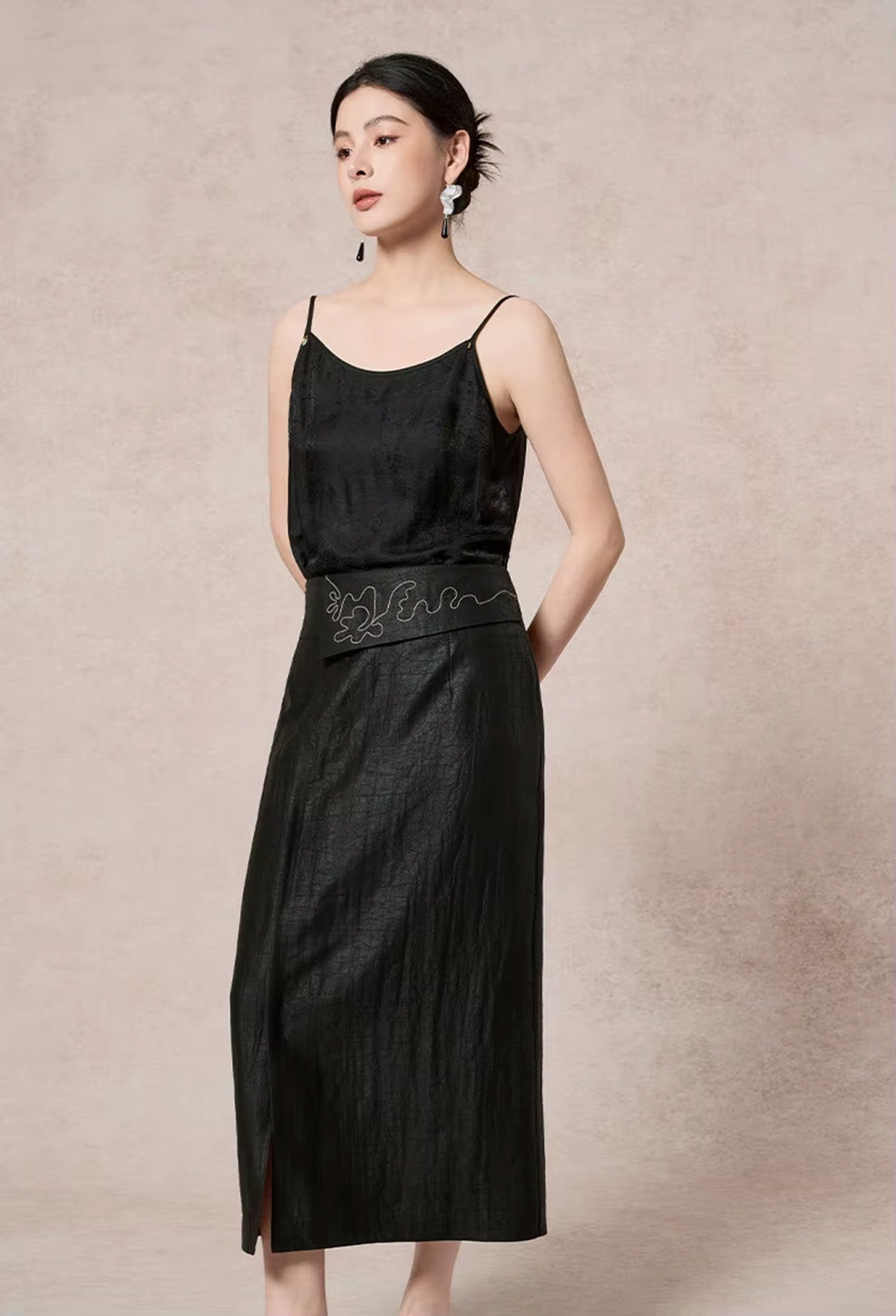 Full-length studio shot of a model standing in the asymmetric column Xiangyunsha silk midi skirt with hands behind her back — From Borcelleclothes.