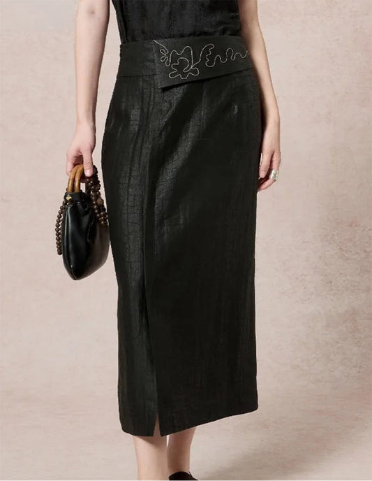 Close-up of a model wearing a structured black Xiangyunsha silk midi skirt with an embroidered overlay waist panel, holding a handbag — From Borcelleclothes.