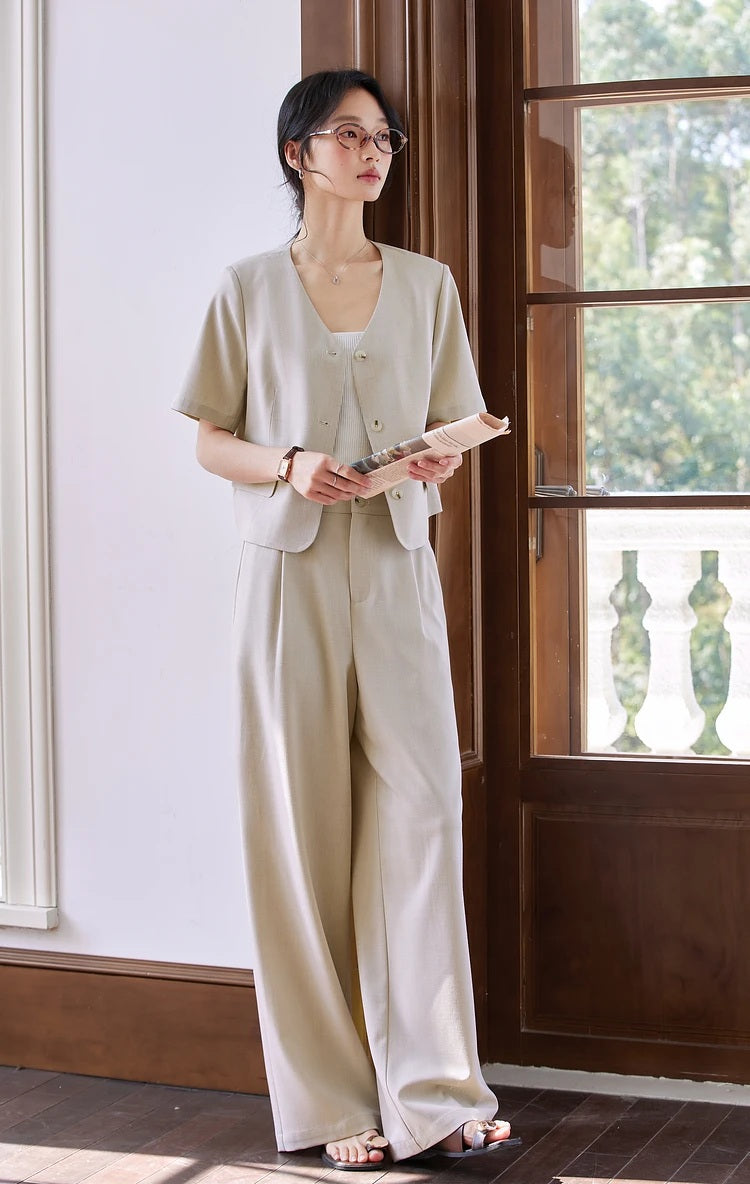 Woman wearing the alabaster two-piece set, casually holding a folded newspaper. From Borcelleclothes.
