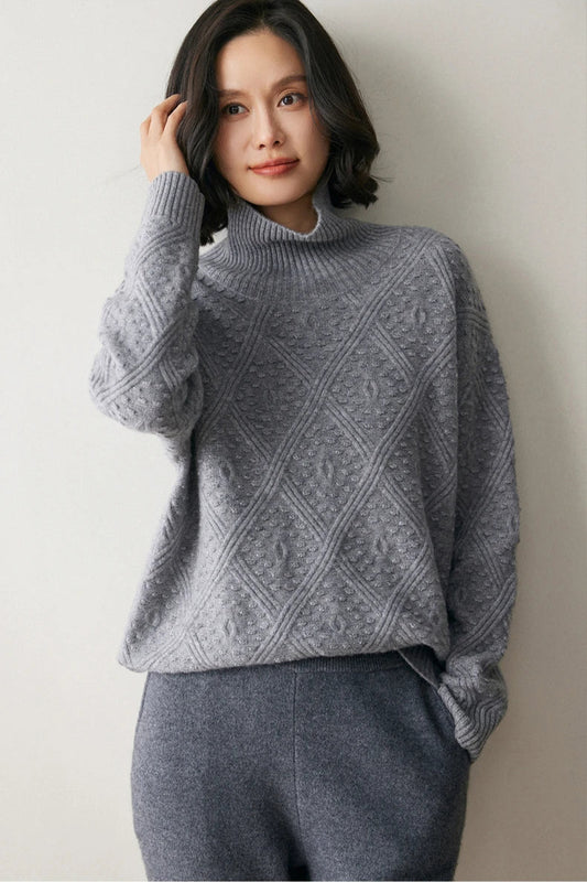 Model adjusting her hair while wearing a French Grey cashmere sweater with a diamond motif and embossed bobble stitches — From Borcelleclothes.