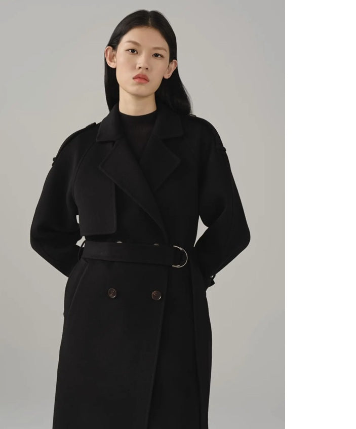 Model wearing the women's cashmere trench coat in Onyx with hands behind the back, showcasing the coat's refined details and elegant fit. From Borcelleclothes.