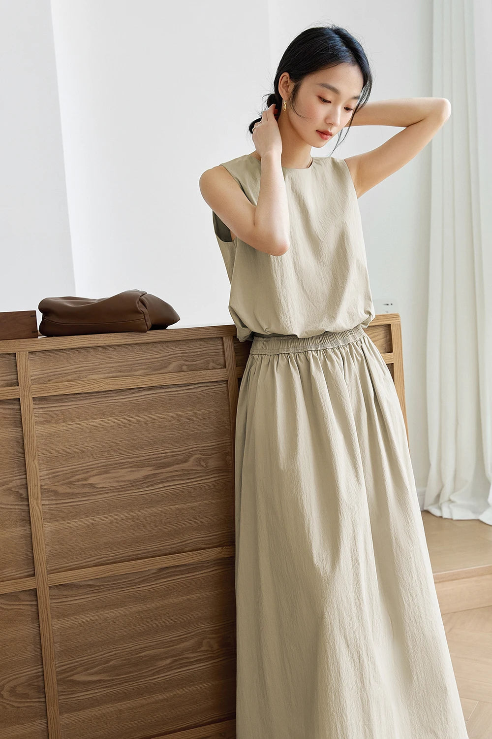 Model adjusting her hair with both hands — the sleeveless crinkled top lifts softly, revealing the gathered hem. From Borcelleclothes.