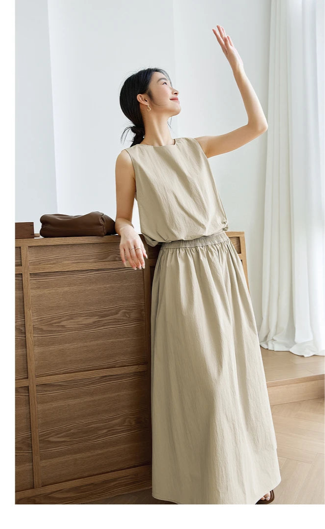 Model leaning against a dresser in Coral Reef outfit — soft folds of the long skirt accentuated in stillness. From Borcelleclothes.