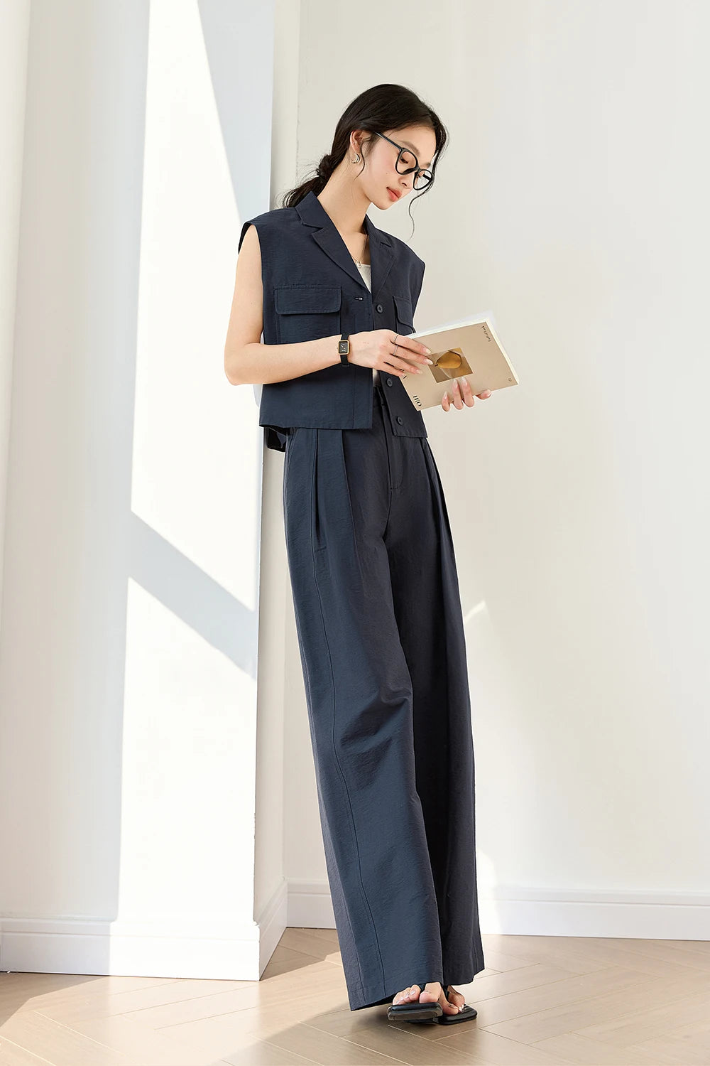 Woman in Mirage two-piece outfit reading a magazine — stillness and focus framed by strong tailoring. From Borcelleclothes.