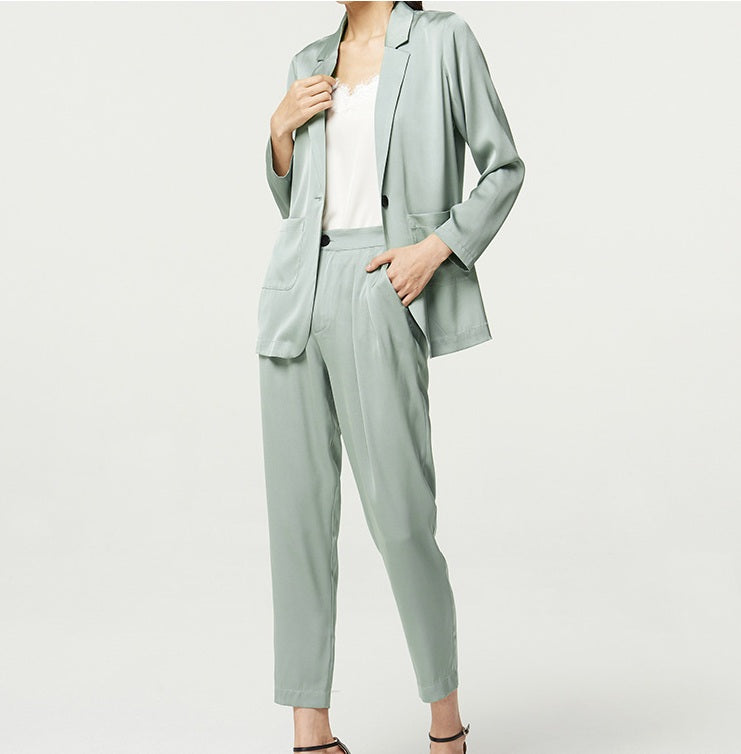 Model in the Nebula silk satin set gently touching the blazer — a pale, cooling tone captured in a quiet gesture. From Borcelleclothes.