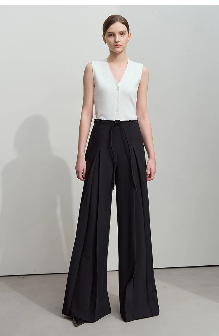 Women’s tailored draped trousers in Onyx, featuring deep sculptural pleats and soft belt loops, styled with minimalist top and relaxed posture. From Borcelleclothes.