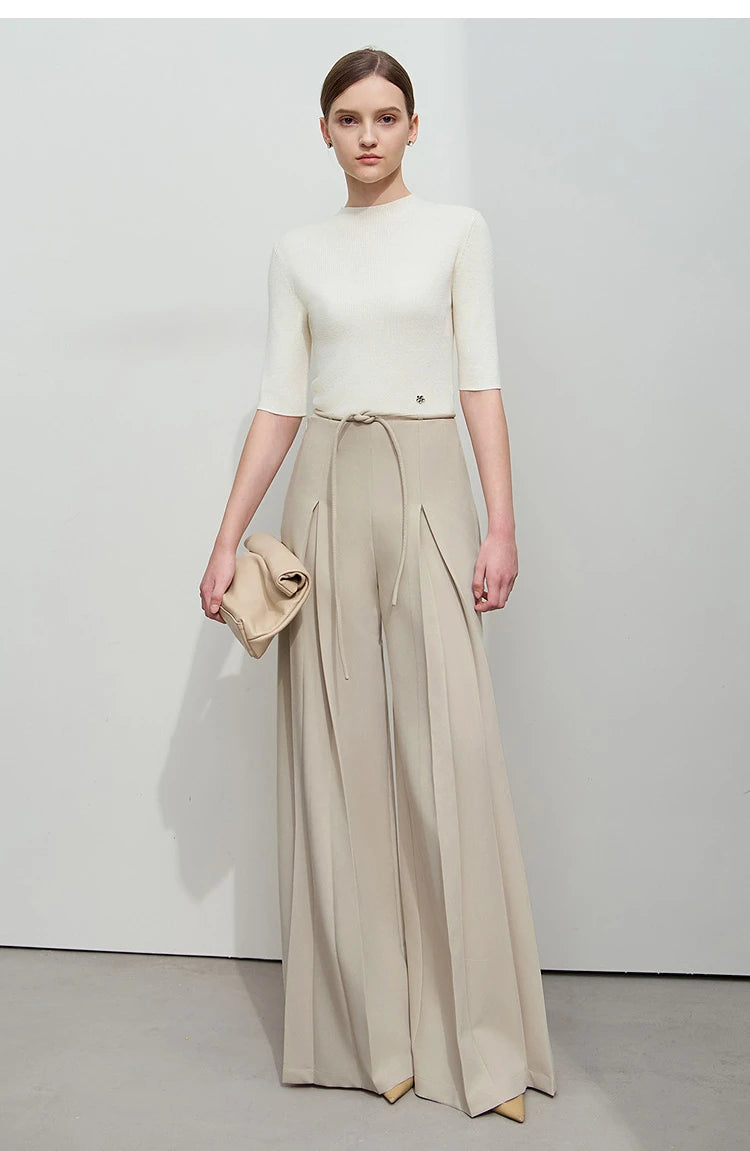 Women’s tailored draped trousers in Silk, featuring deep sculptural pleats and soft belt loops, styled with minimalist top and relaxed posture. From Borcelleclothes.