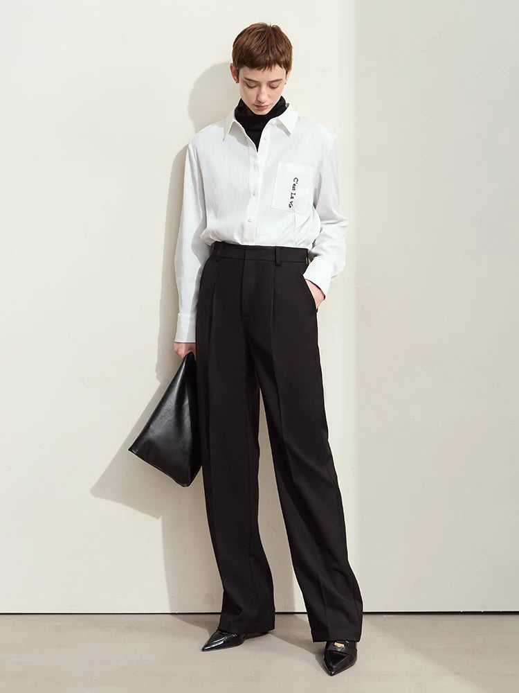 Model wearing tailored loose-fitting trousers in Onyx, holding an oversized bag — contrast between clean lines and voluminous accessory. From Borcelleclothes.