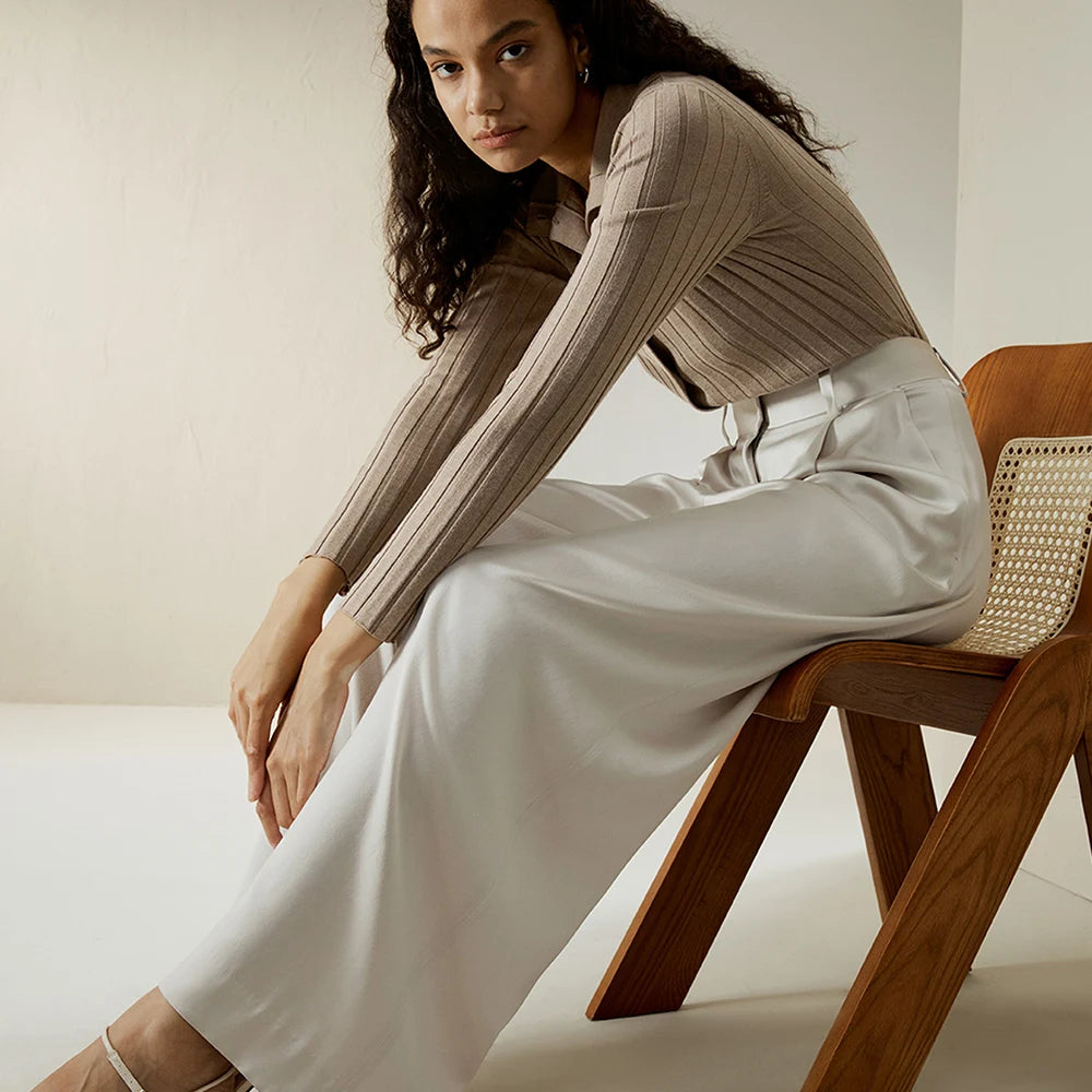 Model seated in Platinum silk trousers, hands resting below knees, emphasizing relaxed confidence. From Borcelleclothes.