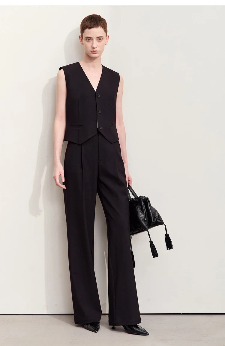 A woman wearing minimalist wool-blend trousers in Onyx, holding a matching bag. — From Borcelleclothes.