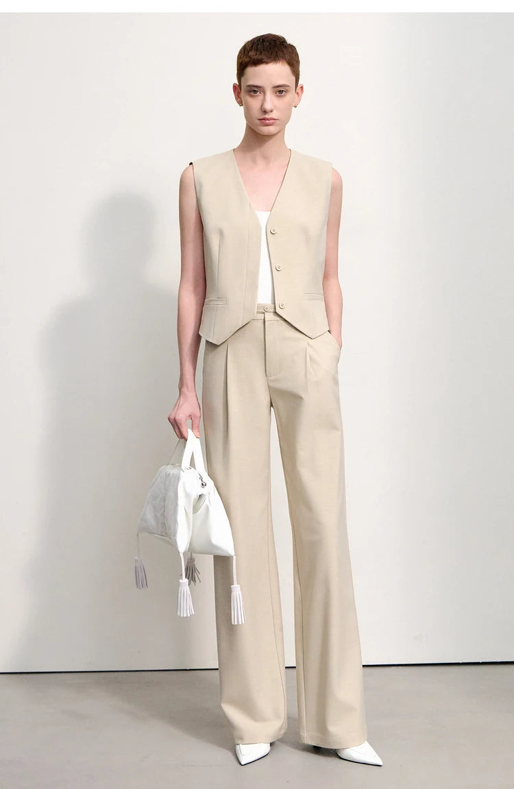 A woman wearing wool-blend minimalist trousers in Soft Amber, holding a white bag. — From Borcelleclothes.