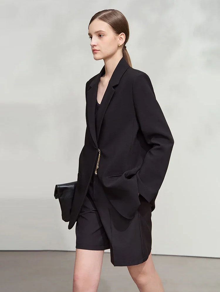 Woman with hand in shorts pocket wearing Onyx wrap blazer with golden pendant – From Borcelleclothes.