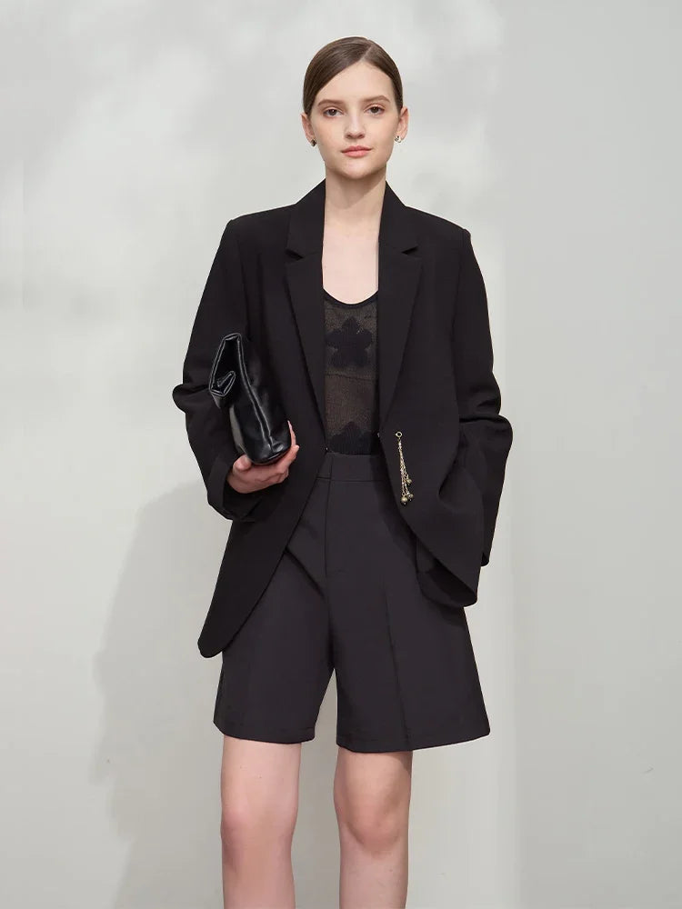 Woman holding bag with hand in shorts pocket wearing Onyx wrap blazer with golden pendant – From Borcelleclothes.