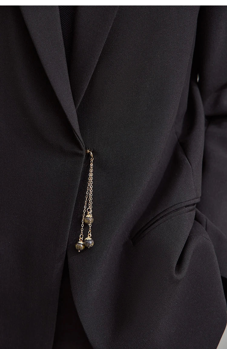 Close-up of golden pendant detail on Onyx wrap blazer – From Borcelleclothes.