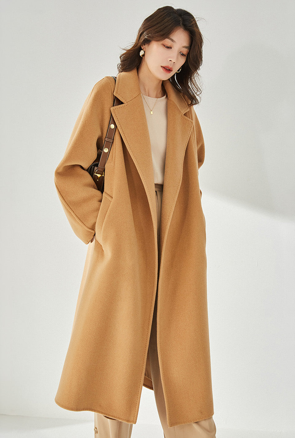 A model wearing the Women's Wrap Coat Redefined in Brown Sugar, looking downward, highlighting the coat’s sophisticated drape and effortless wearability. From Borcelleclothes.
