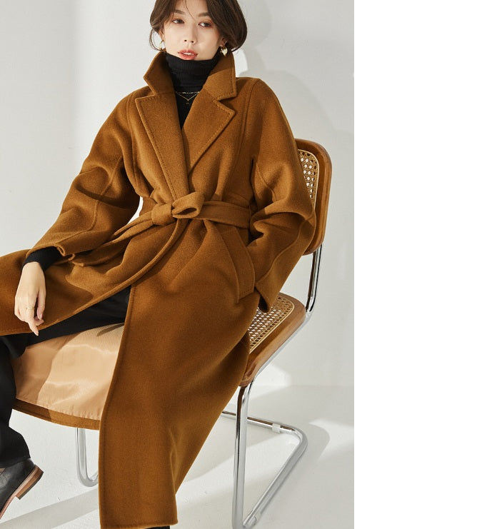 A model wearing the Women's Wrap Coat Redefined in Rich Gold, elegantly seated in a chair, showcasing its fluid silhouette and structured details. From Borcelleclothes.